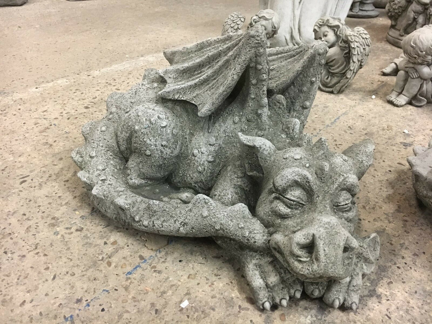 Close-up of sleeping stone baby dragon statue with textured wings and curled tail, part of a weatherproof garden ornament pair.