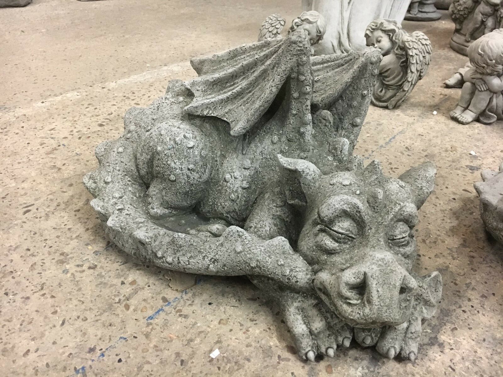 Close-up of sleeping stone baby dragon statue with textured wings and curled tail, part of a weatherproof garden ornament pair.