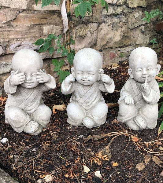 Baby Monk Ornaments - See, Hear, Speak No Evil Set in stone finish, displayed in a garden setting with rustic stone wall background.