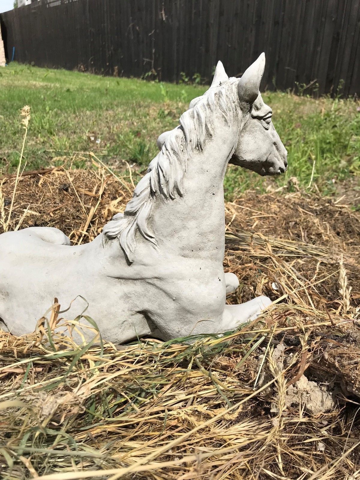 Back side view of Stone Resting Horse Statue - Garden Ornament placed on straw, showing its solid build and outdoor suitability.