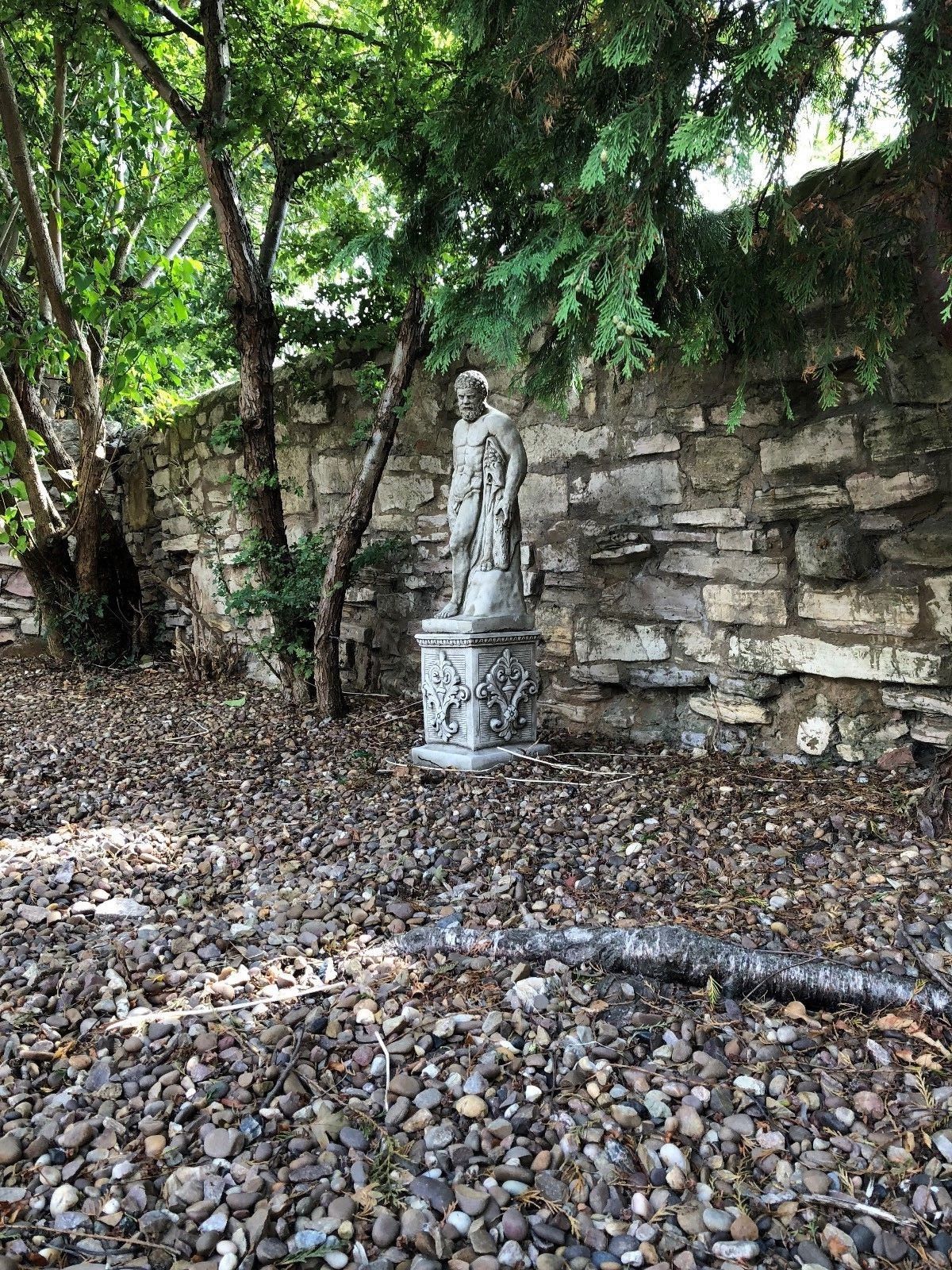 Distant view of Hercules garden statue in shaded outdoor area, standing on ornate limestone plinth for classic appeal.
