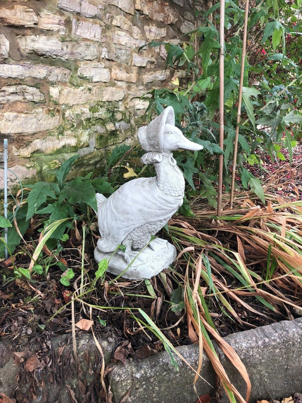 Side view of stone duck ornament in bonnet, nestled in a garden bed. Adds character and charm to patios or flowerbeds.
