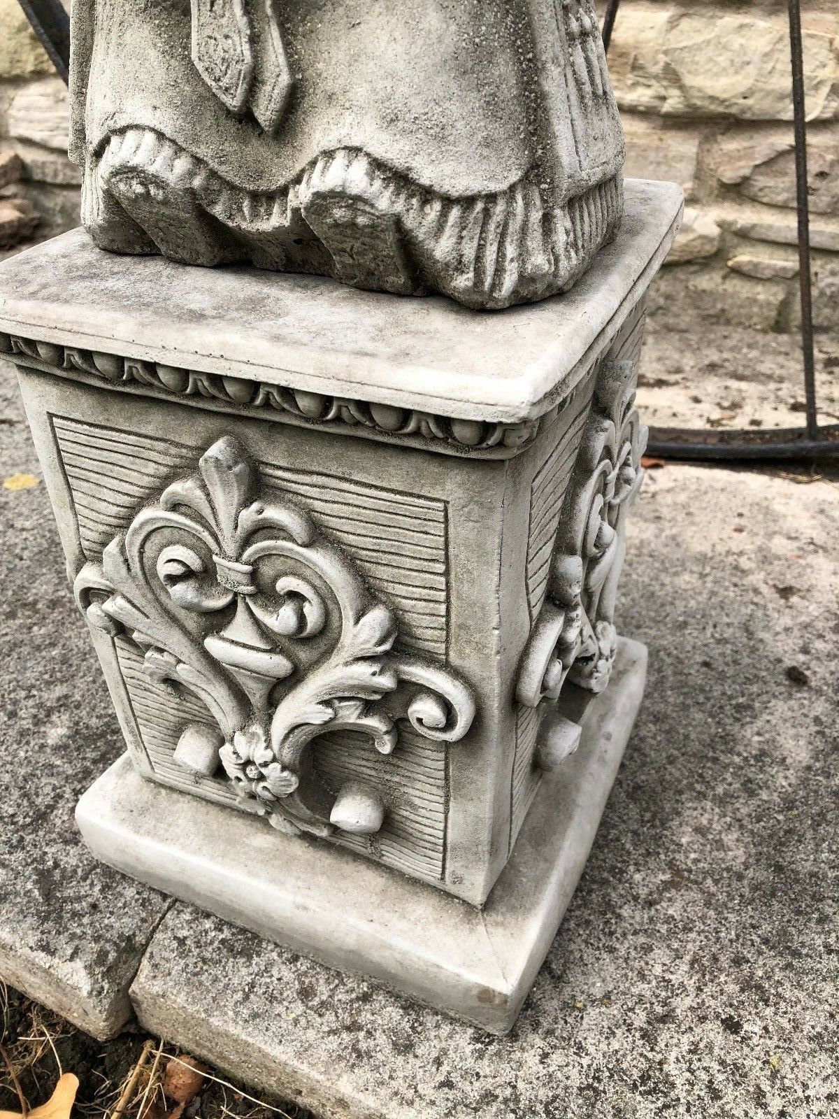 Close-up of decorative limestone plinth base supporting Hercules statue, featuring floral and scrollwork carvings.