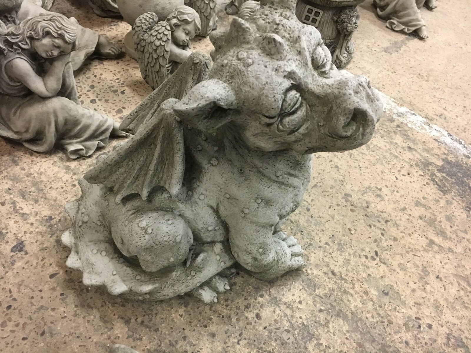 Top view of sitting stone baby dragon statue with closed eyes and textured body, ideal for whimsical garden decor.