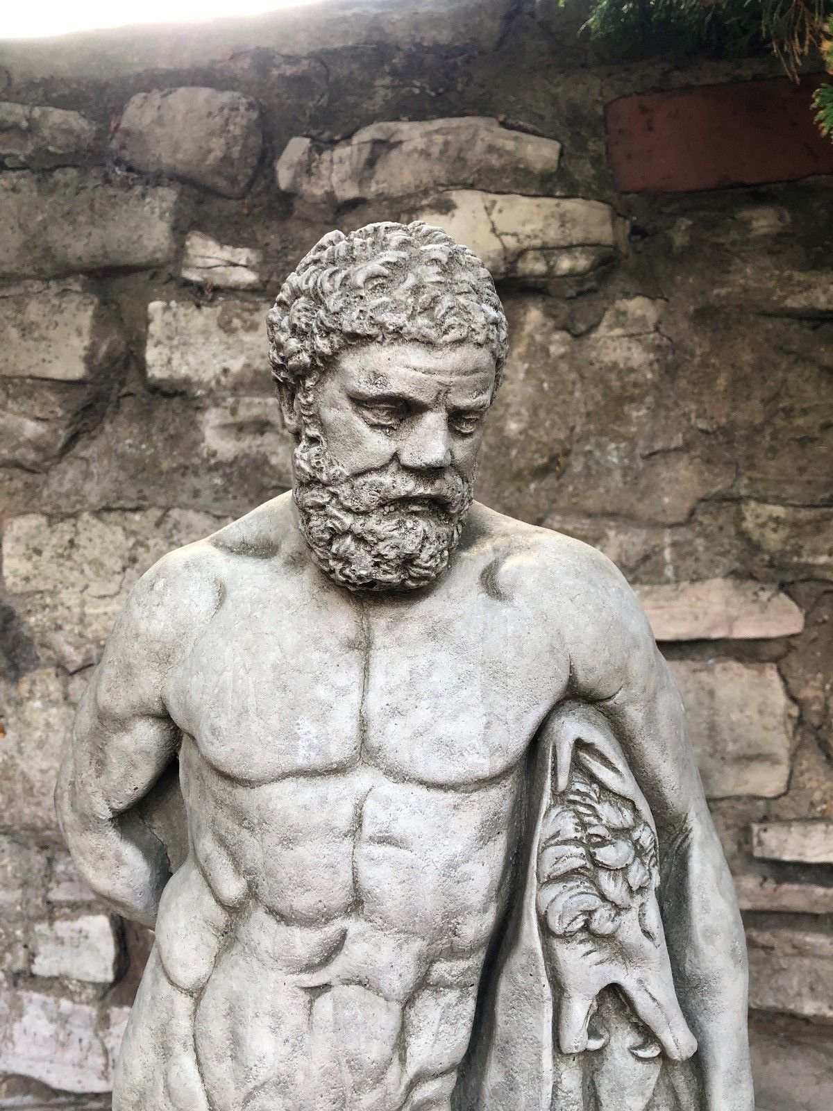 Detailed facial view of Hercules statue with curly beard and lion skin, crafted in antique grey limestone for garden display.