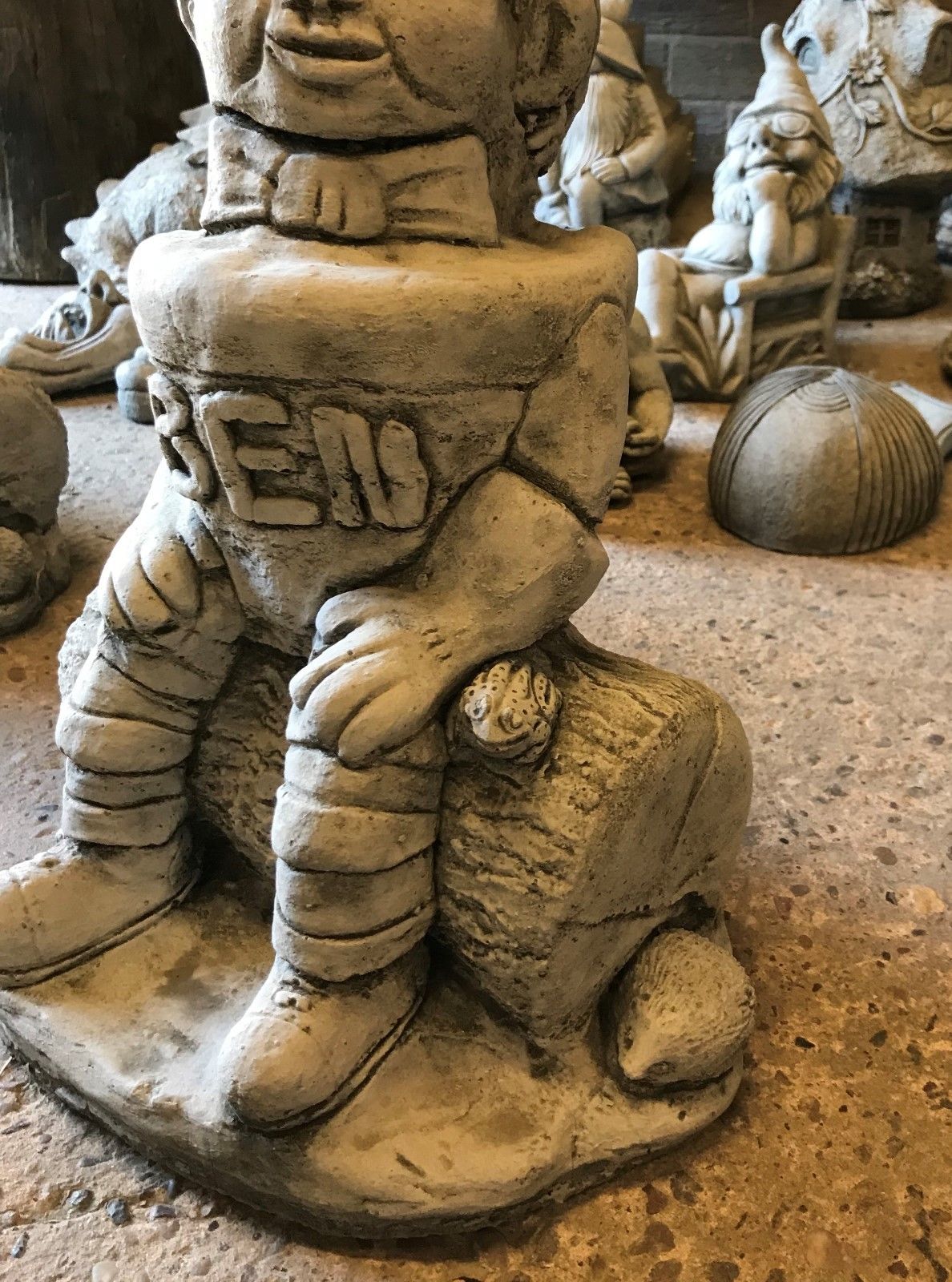 Close-up of the Stone Ben statue's base, showing a carved log with a frog and hedgehog, adding charm to garden landscapes.
