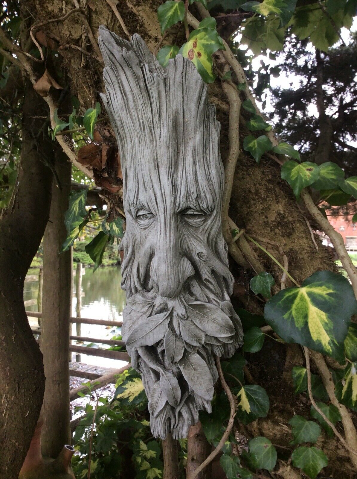 Handmade Greenman garden ornament with bark-like texture and leaf details, blending into a natural garden setting.