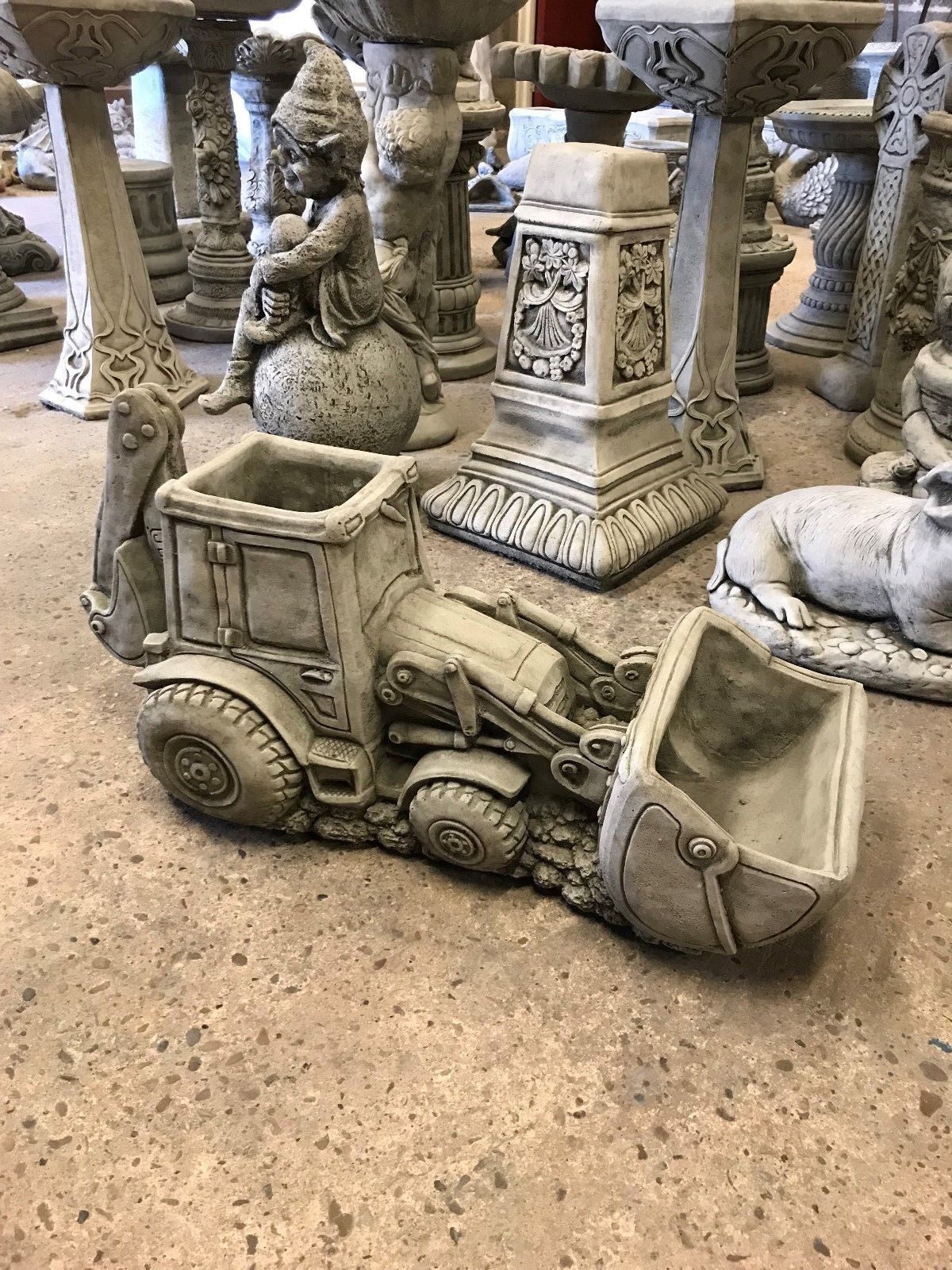 JCB Shovel Digger Planter - Garden Feature | Heavy & Durable concrete digger planter displayed indoors among other garden statues and ornaments.