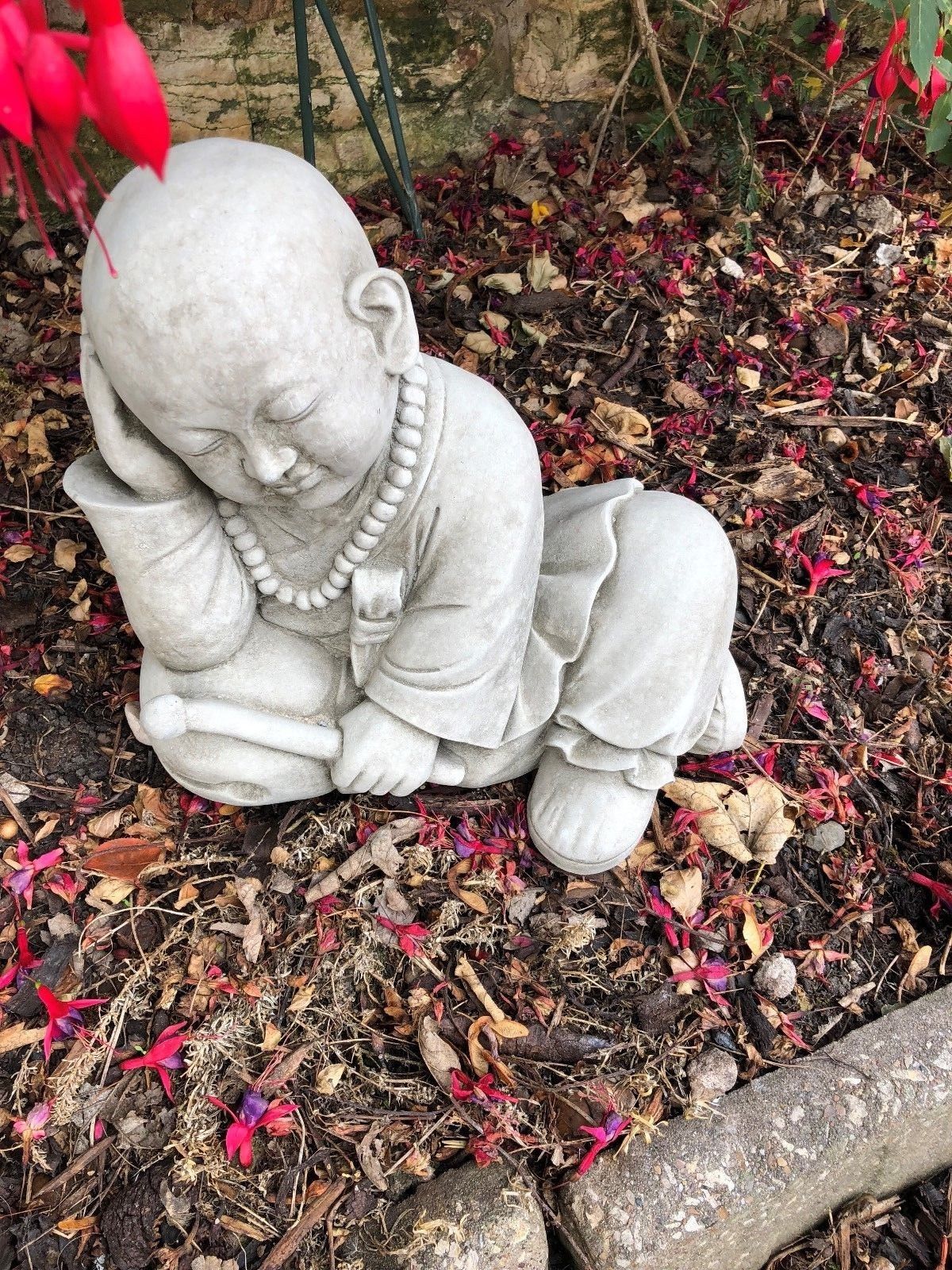 Limestone Resting Monk Sculpture Garden Ornament surrounded by petals, ideal for zen gardens, patios, or Buddhist-inspired outdoor décor.