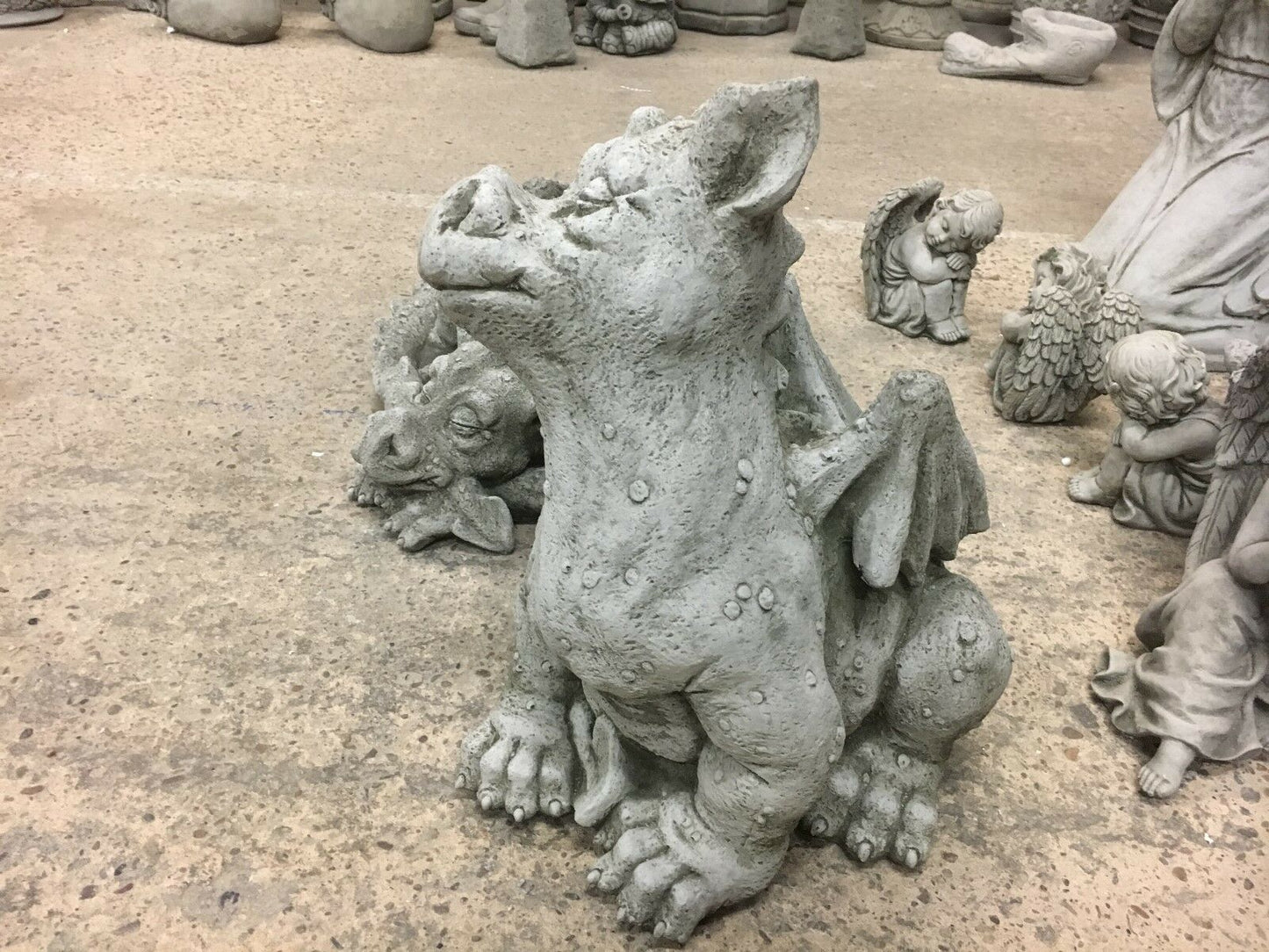 Front view of sitting stone baby dragon statue with smiling expression and antique finish, perfect for lawn or patio display.