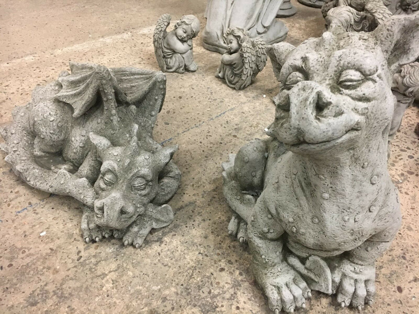 Pair of stone baby dragon statues, one sleeping and one sitting, crafted for weatherproof garden ornamentation with antique charm.