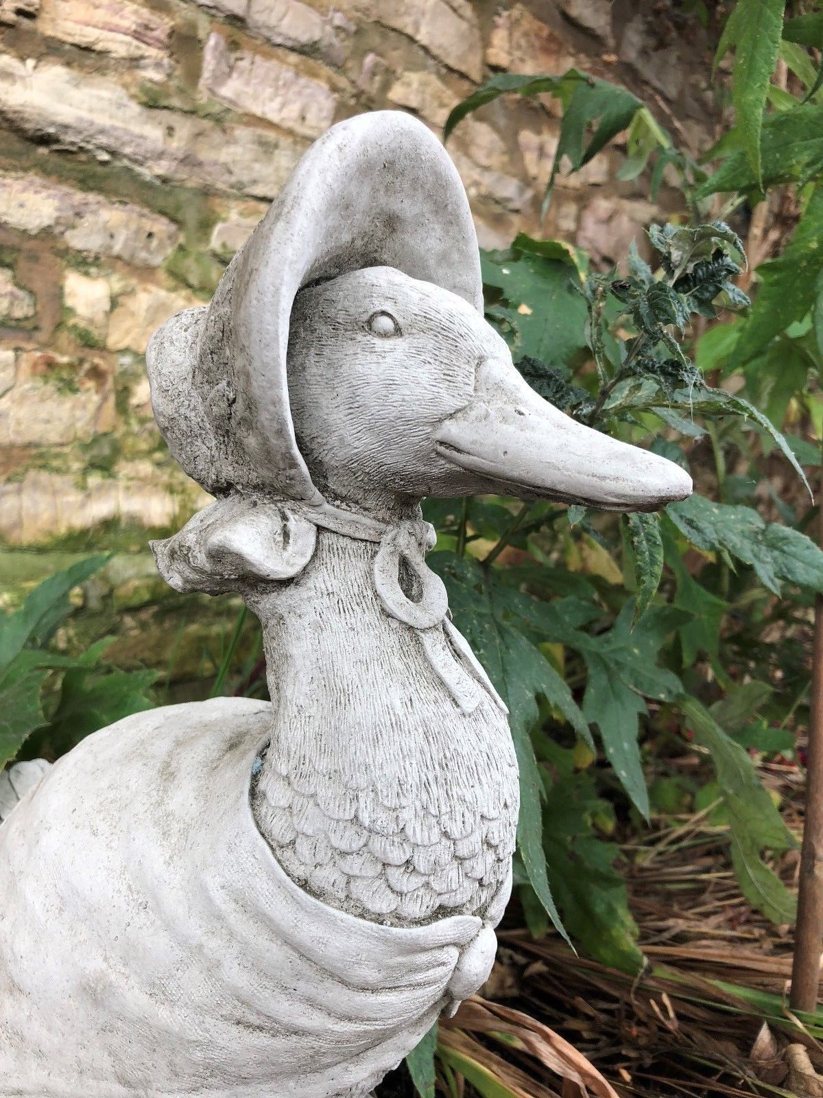 Close-up of duck garden ornament with bonnet, highlighting stone craftsmanship. A charming and durable garden decor piece.