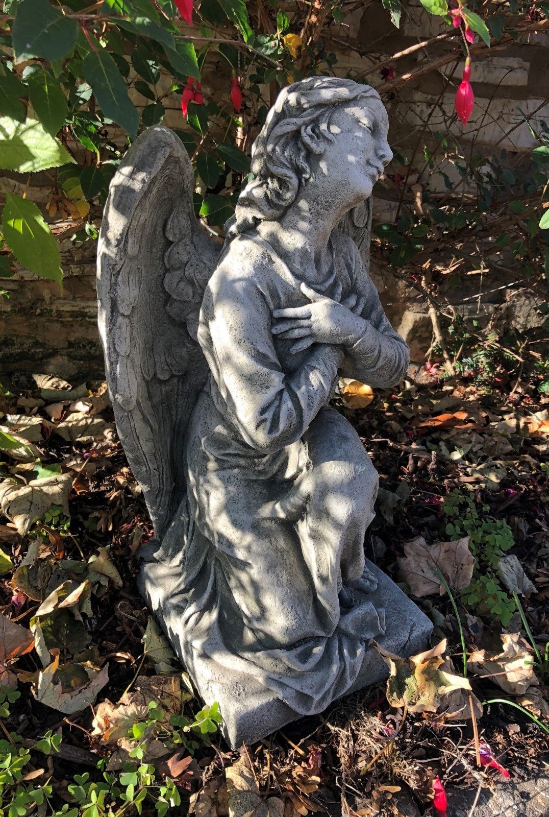 Durable Stone Kneeling Angel Garden Statue with Arms Crossed, ideal for lawn or patio decoration, surrounded by autumn leaves and flowers.