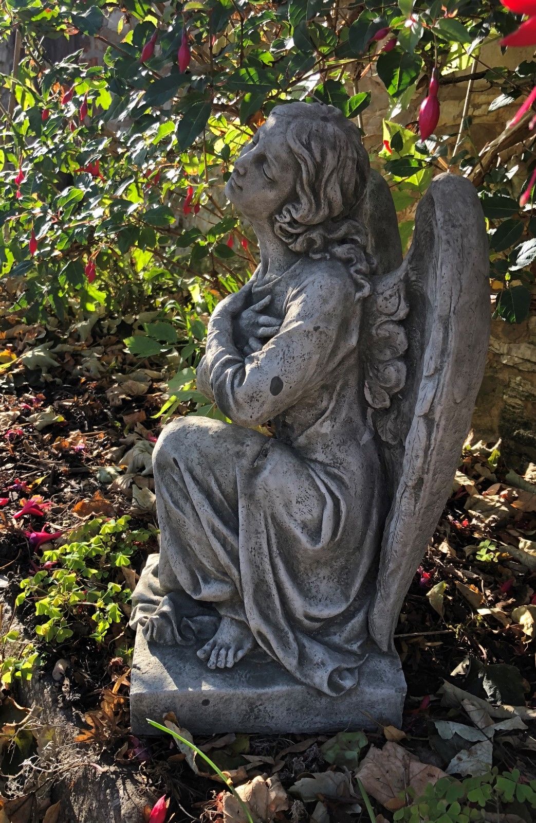 Profile view of Angel Garden Statue - Stone Kneeling Arms Crossed on a stone base, ideal for memorial gardens or decorative landscaping.