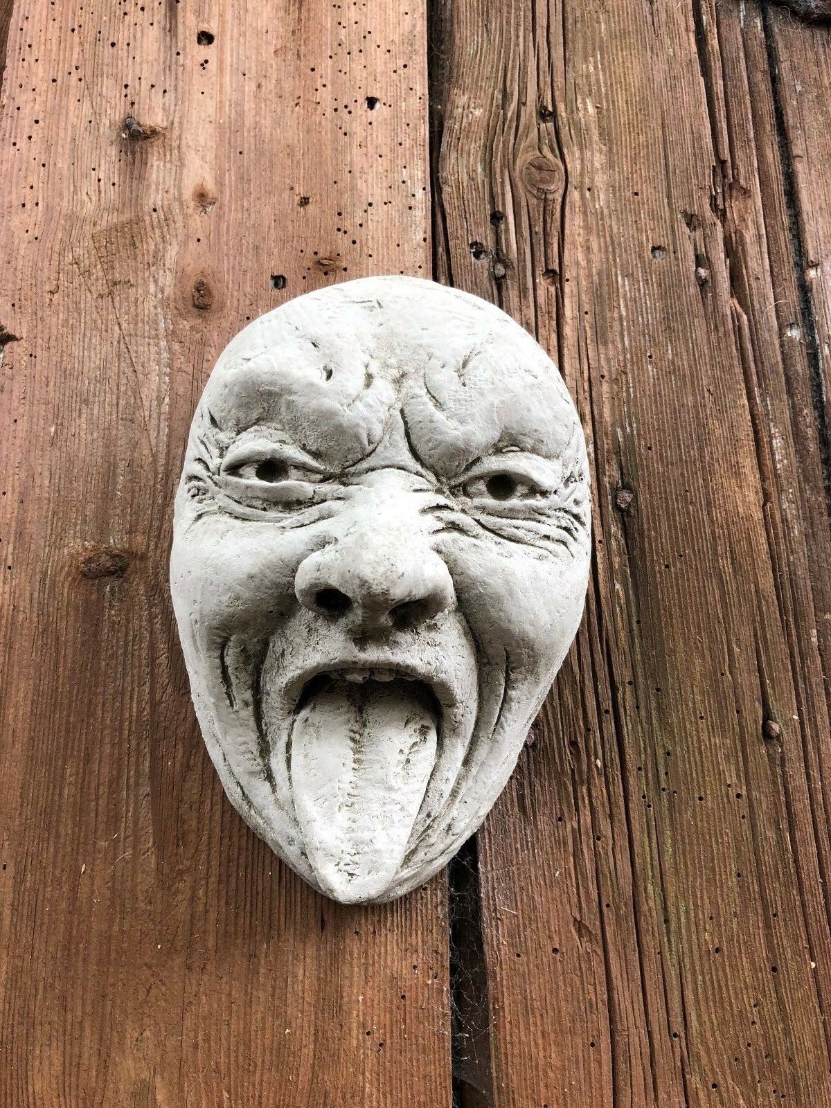 Front view of Stone Tongue Out Face Plaque on wooden background, adds humor to garden décor. Made from solid limestone.
