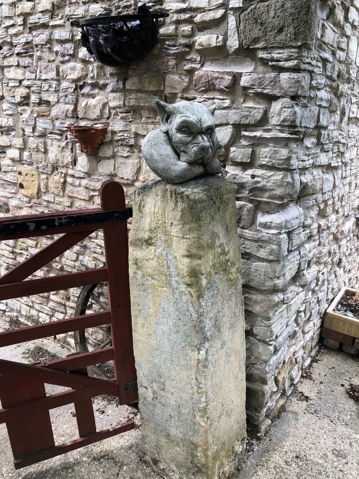 Stone Gargoyle Dog Finial on weathered pillar near wooden gate, perfect as a durable and decorative garden ornament.