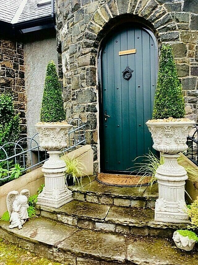 Close-up of Bacchus design urn planters with topiary trees on stone steps, showcasing detailed craftsmanship and garden charm.
