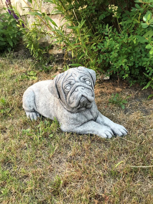Stone Pug Sculpture - Garden Ornament made from fine limestone, resting on grass with detailed texture, ideal for outdoor garden decor.