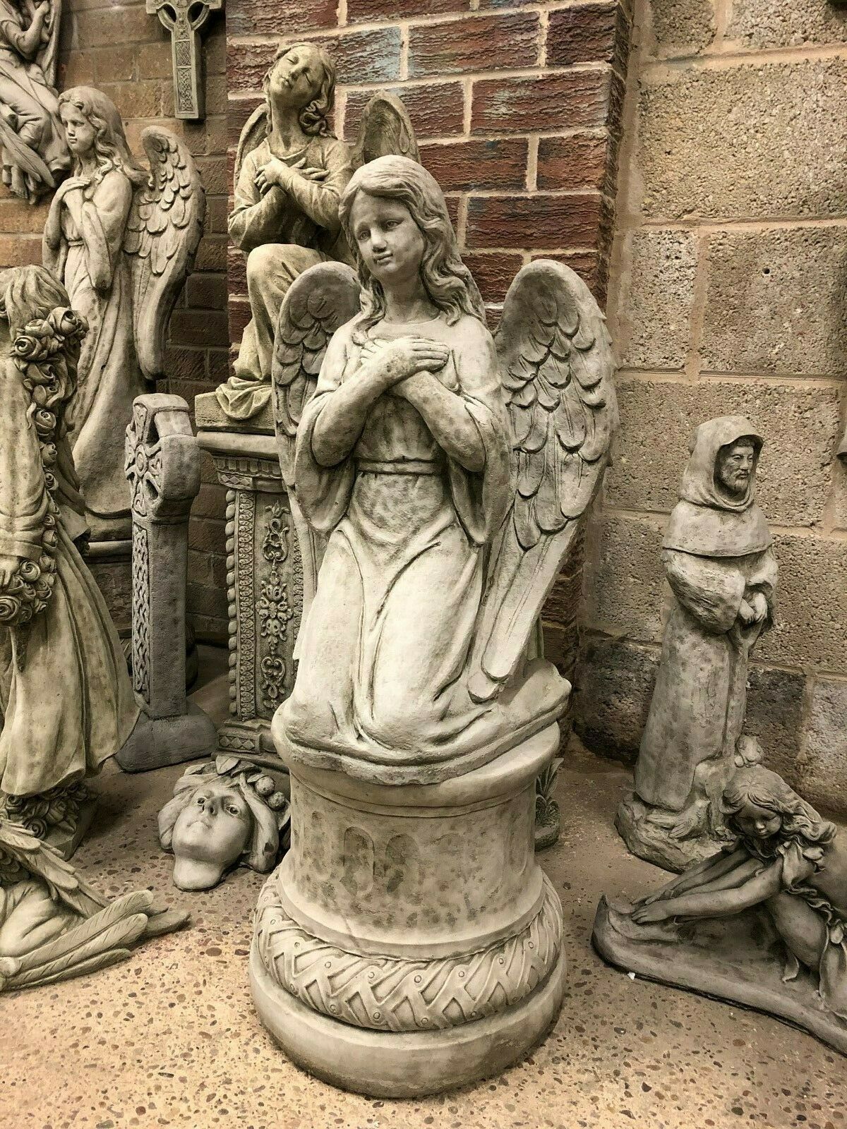 Solid stone kneeling angel sculpture with detailed wings and antique finish, perfect for outdoor garden ornament or patio decoration.