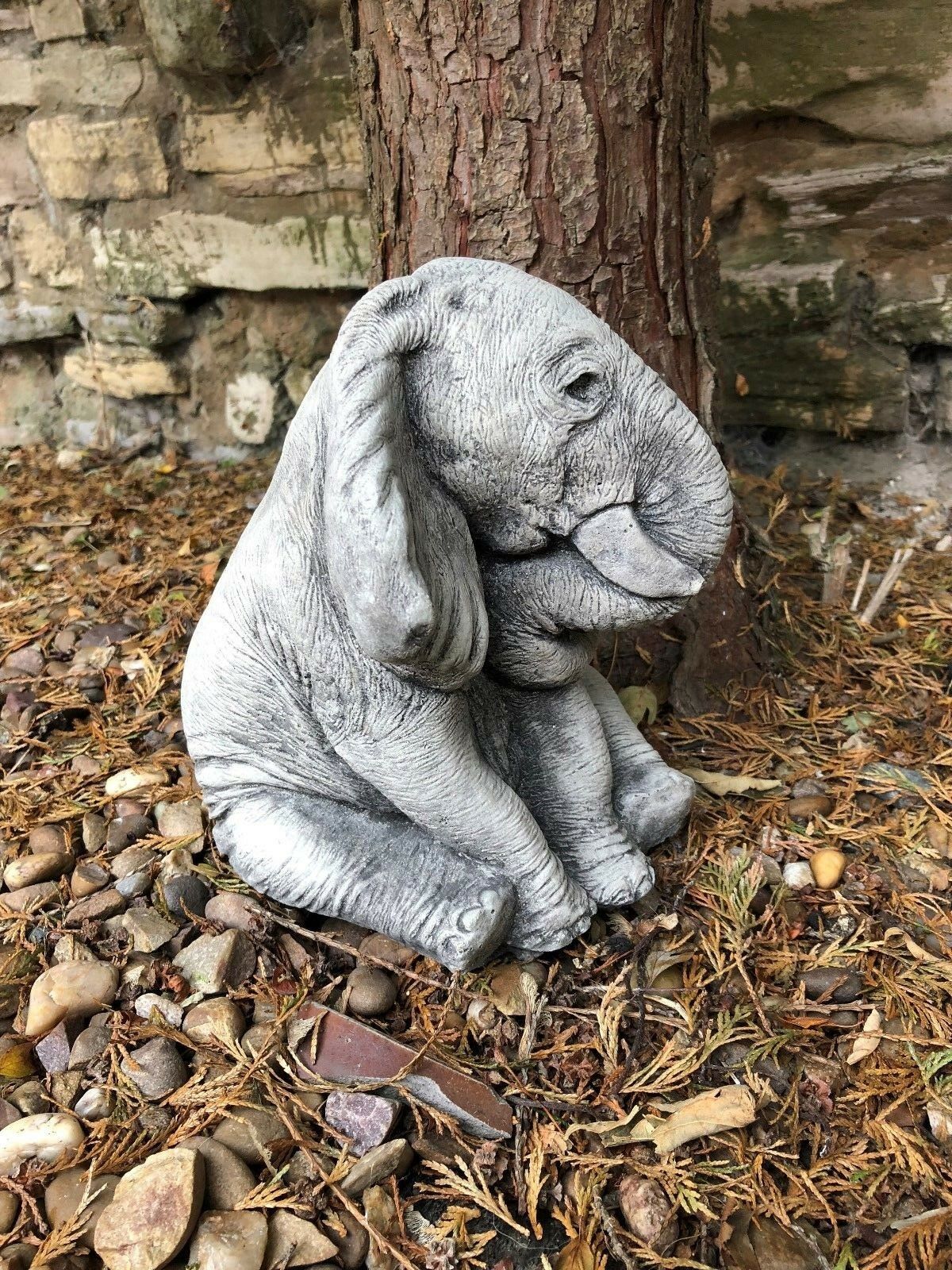Realistic stone baby elephant garden ornament sitting under a tree, ideal for adding character to flower beds or outdoor landscapes.