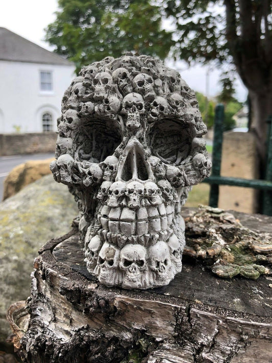 Stone Skull Garden Ornament with intricate mini skull details, placed on a tree stump. Unique outdoor décor with a gothic limestone finish.