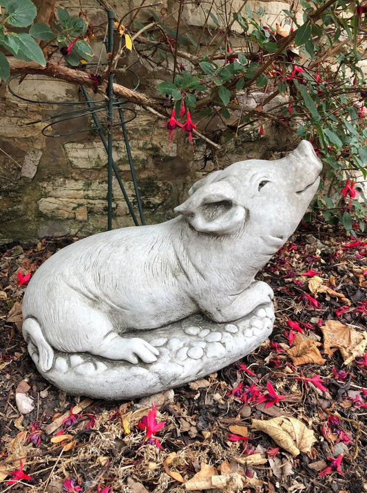 Stone Pig Sculpture Garden Ornament featuring a lazy pig lying on a textured base, ideal for patios or flower beds. Antique grey finish for rustic charm.