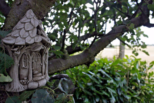 Stone Fairy Garden House wall plaque mounted on a tree, surrounded by lush greenery. Ideal for outdoor garden decor with a magical woodland theme.