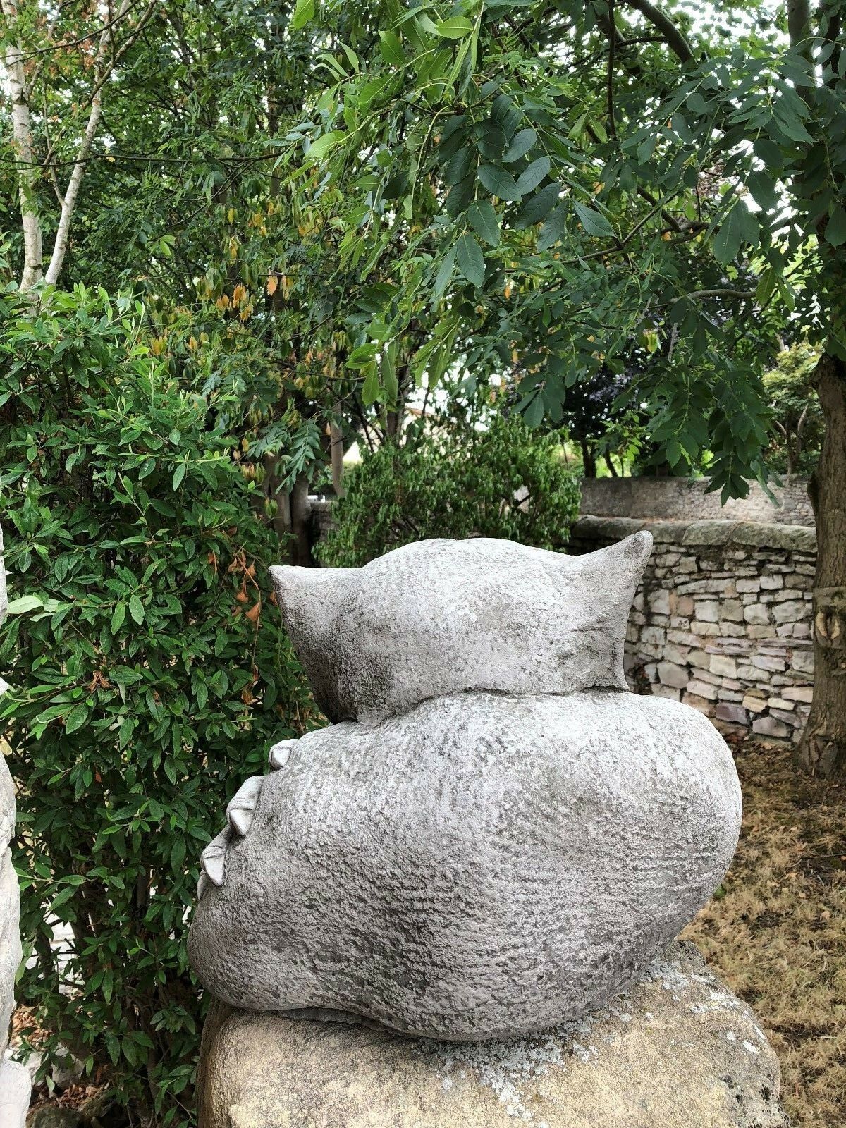 Rear view of Gargoyle Dog Finial - Stone Garden Ornament nestled in a lush garden setting, emphasizing its large and sturdy form.