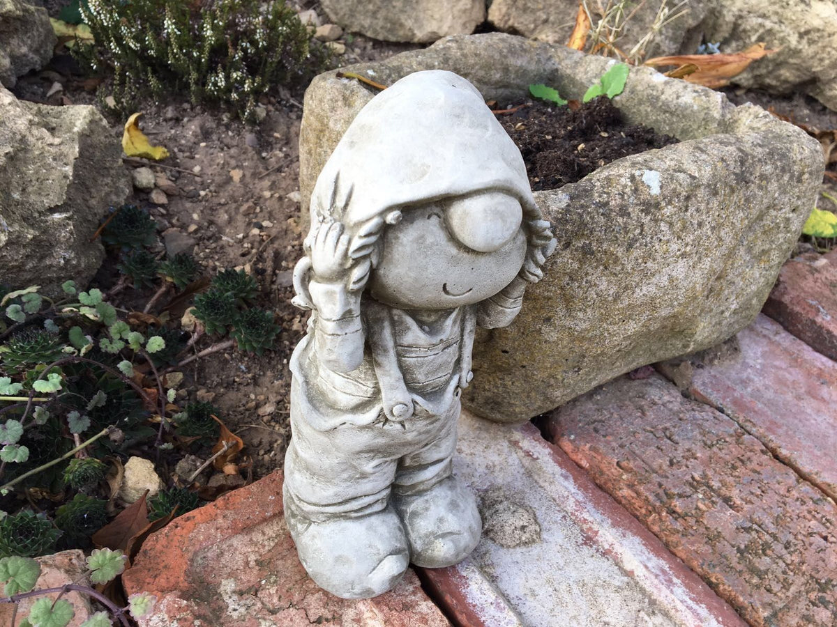 Angled top view of the Stone Boy Garden Ornament in Dungarees near a stone planter. Adds character to any garden or outdoor space.
