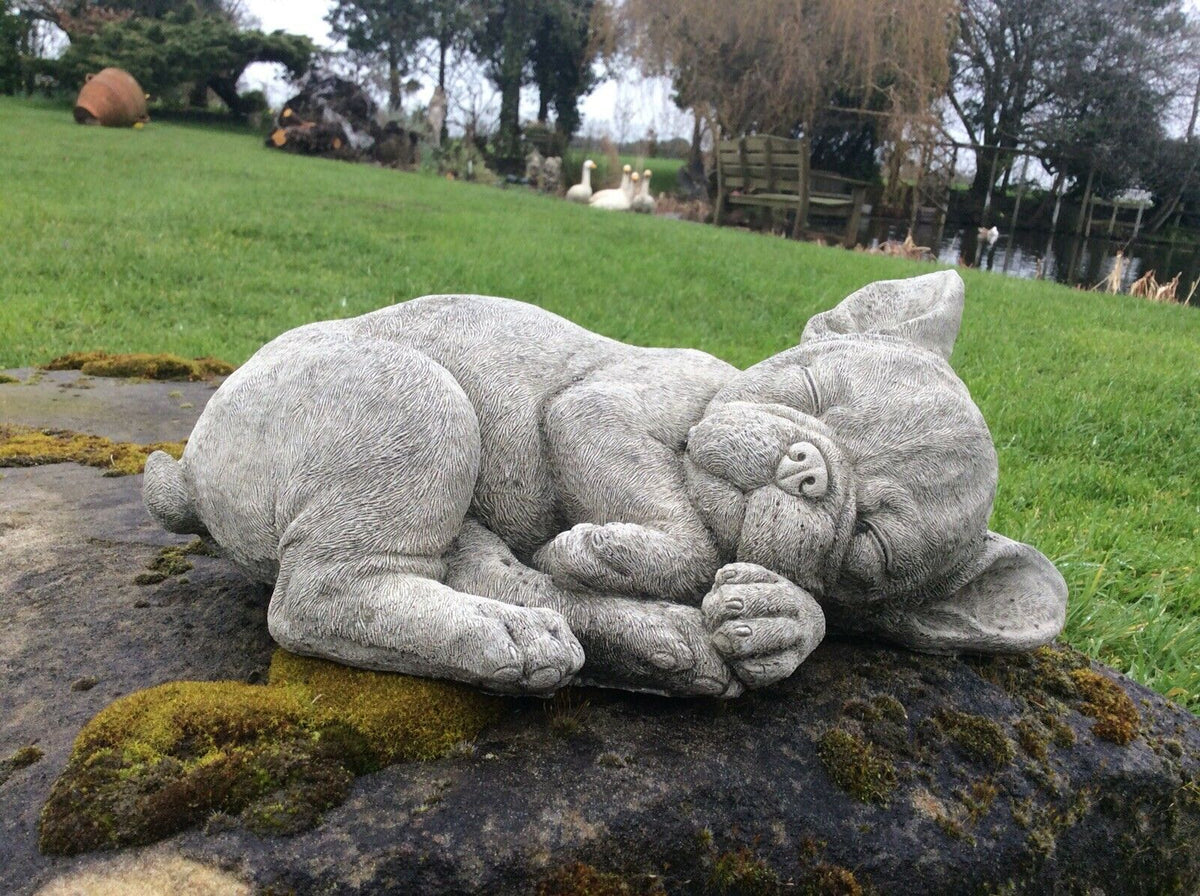 Solid stone sleeping French Bulldog garden sculpture placed on a rock, perfect for patios and decorative outdoor spaces.