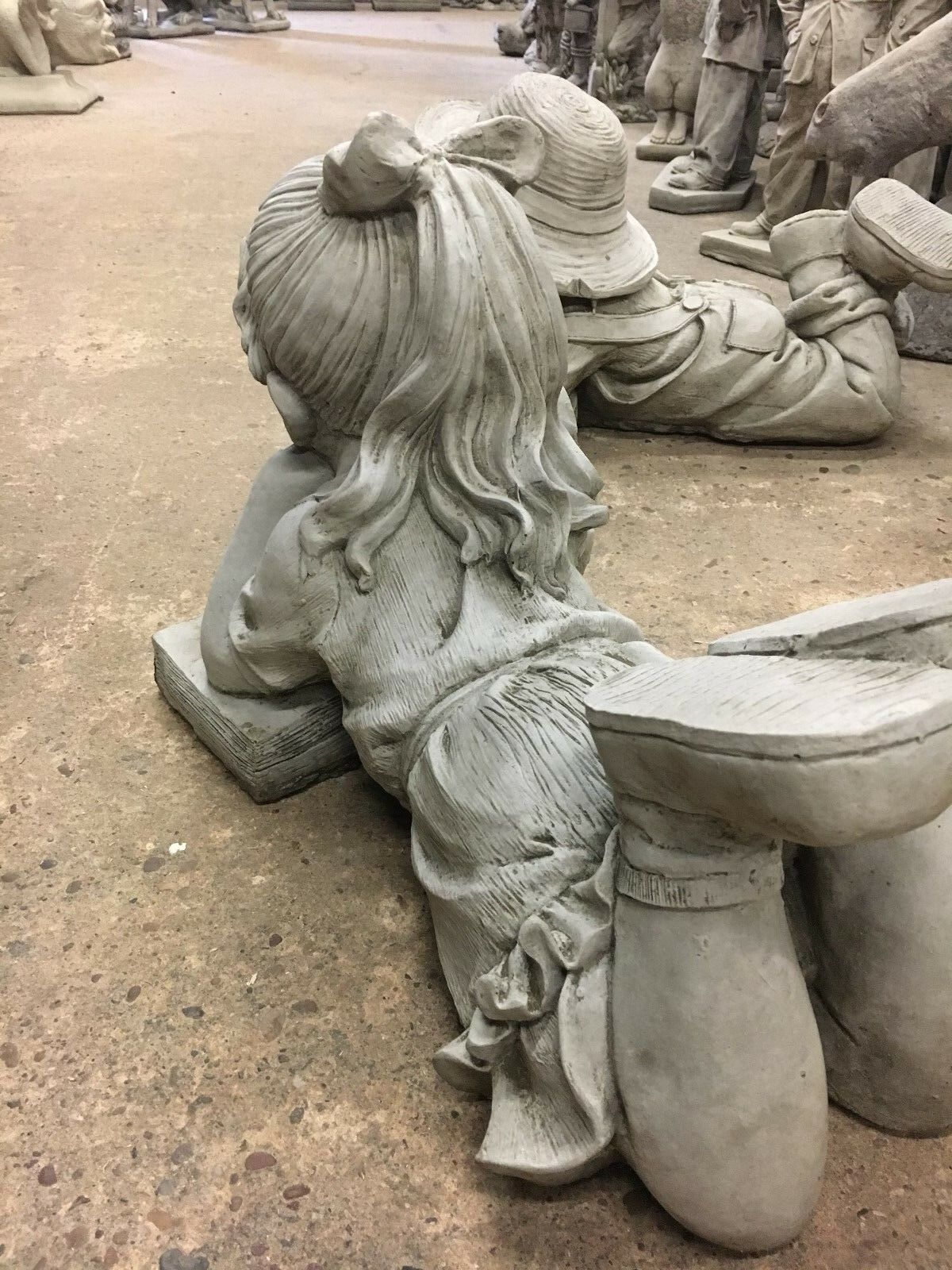 Back view of Reading Girl Statue with ponytail and dress, made from solid stone for long-lasting garden decoration.