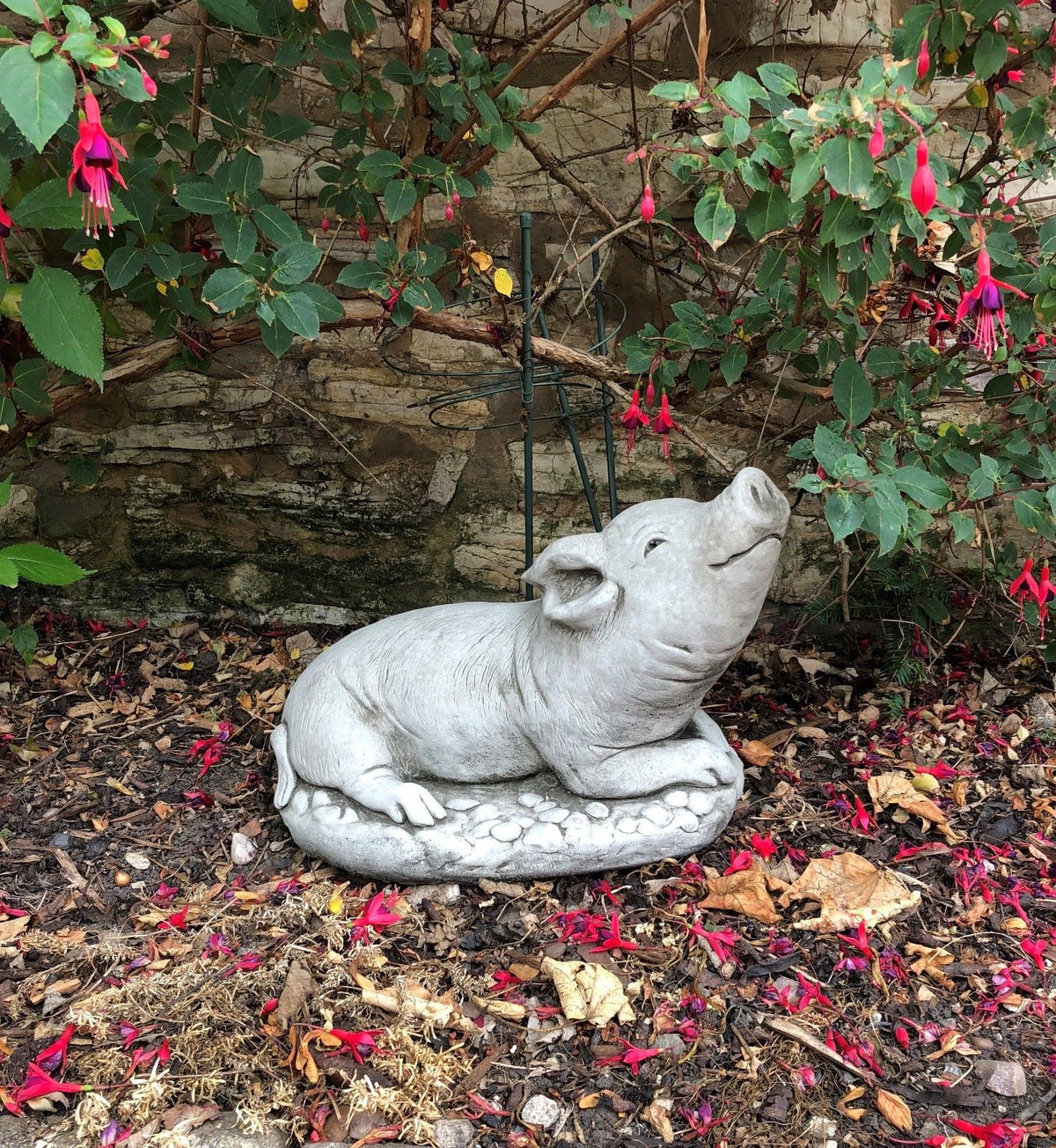 Durable Stone Pig Sculpture Garden Ornament nestled among fallen leaves and flowers. Handmade from limestone with a charming, chubby design.