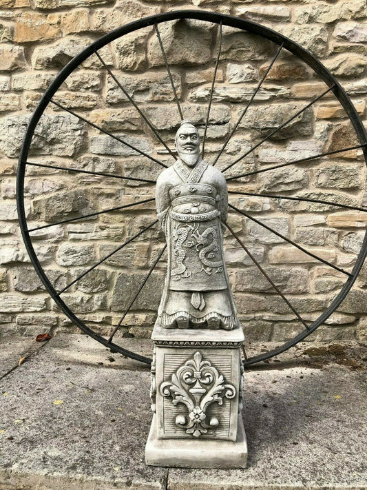 Stunning Stone Zhan Shi Warrior Garden Plinth Statue displayed outdoors with a rustic stone wall and large iron wheel backdrop, ideal for garden decor.